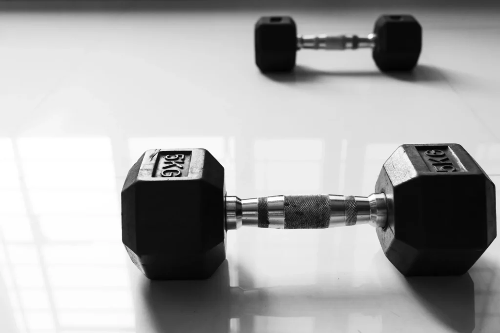 Black hexagonal dumbbells placed on a clean floor in the Modern Work low-impact gym.