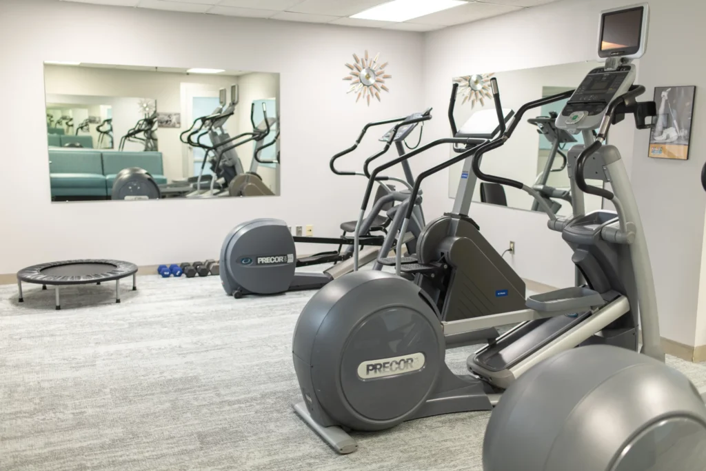 Modern Work Suites fitness area with elliptical machines, a trampoline, hand weights, and mirrors.