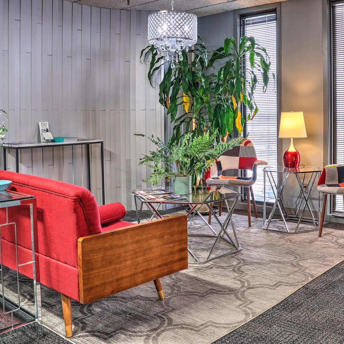 Modern lounge area with a red sofa, colorful chairs, plants, a glass coffee table, and a chandelier, located within the Modern Works office space.