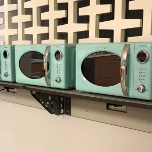 Three mint green retro-style microwave ovens with chrome details on a shelf against a geometric-patterned backdrop located in the Mixx Lounge.