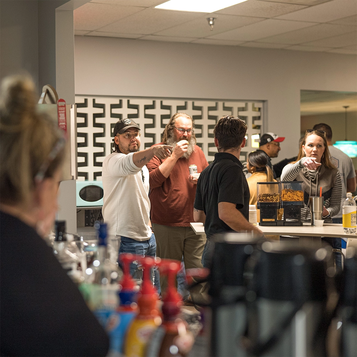 An office break room with individuals gathered around counters, including a man in a white shirt pointing at something, and others socializing where they have office space for rent.