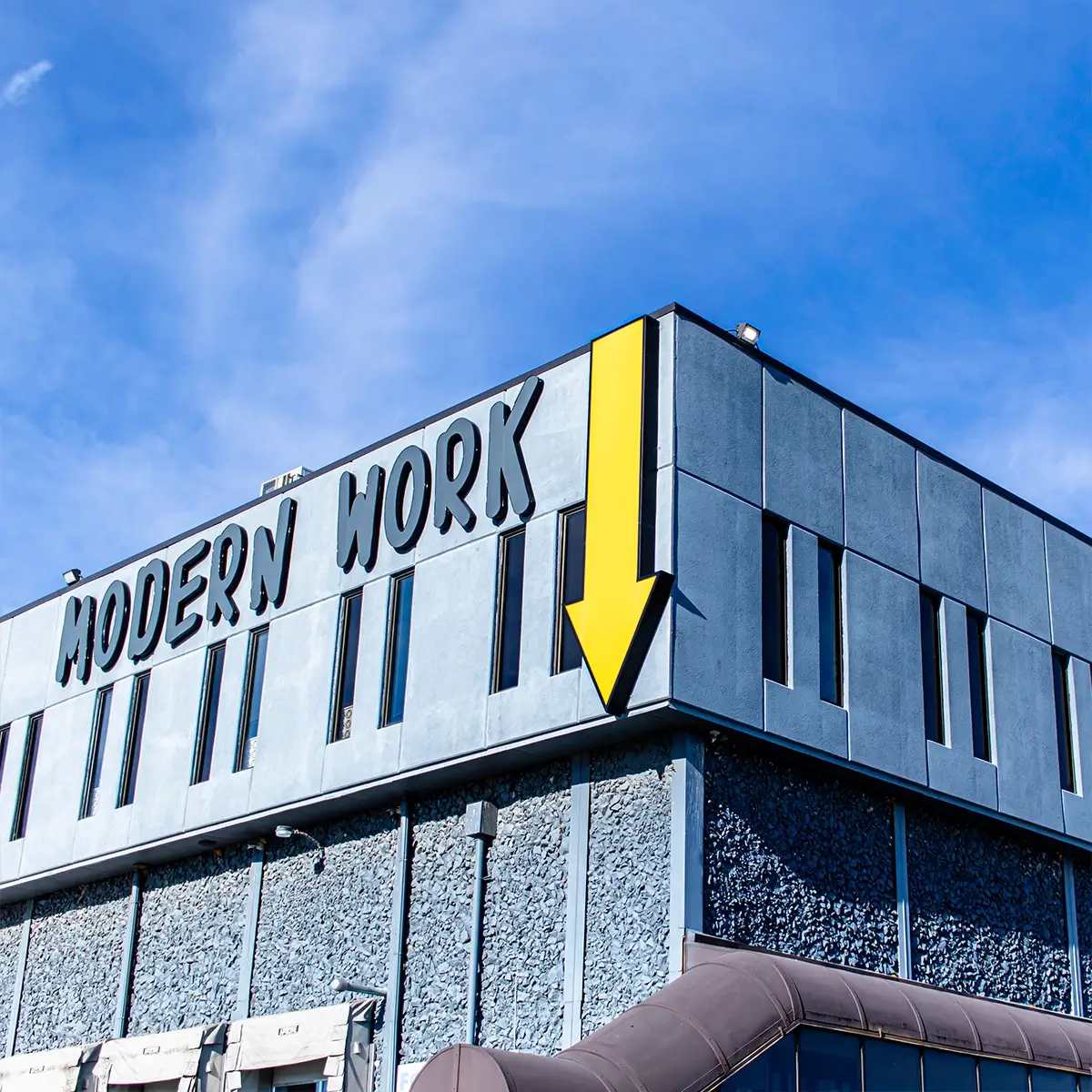 A building with Modern Work in bold letters and a large yellow arrow on the side, set against a clear blue sky, hints at dynamic office space ready to inspire productivity and innovation.